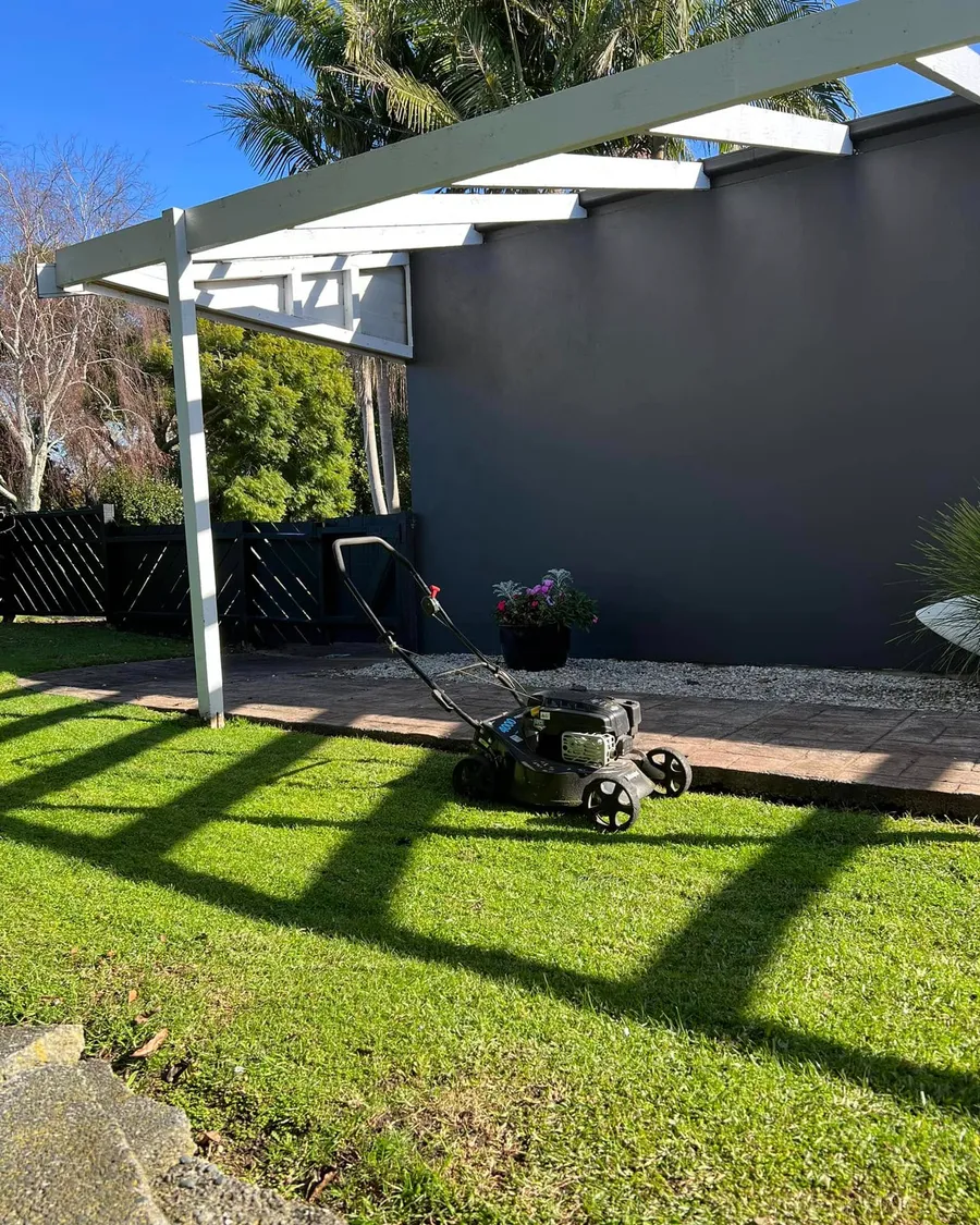 Freshly mowed back lawn under a white pergola beside a dark house in Manly, Whangaparāoa