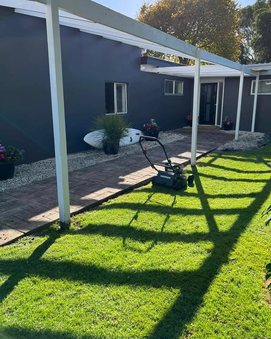 Freshly mowed lawn with crisp edges along a brick path beside a dark house in Whangaparāoa