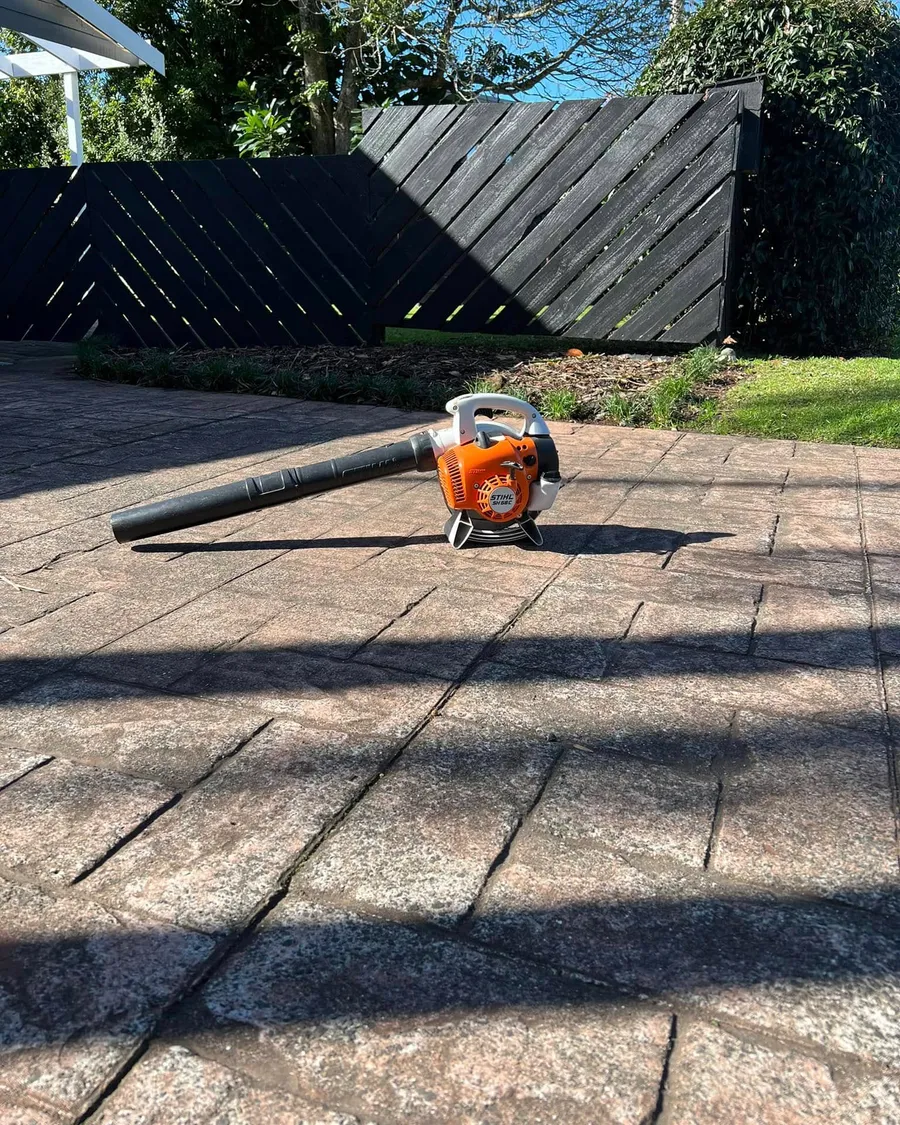 Blower on a clean paved patio in front of a black fence and hedge on the Hibiscus Coast